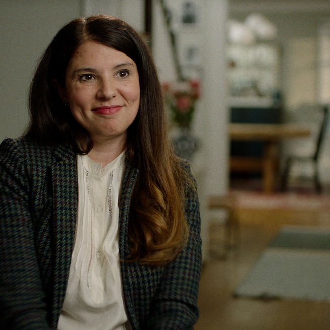 Audrey, actual patient with lung cancer, in a plaid blazer sitting in a living room, smiling