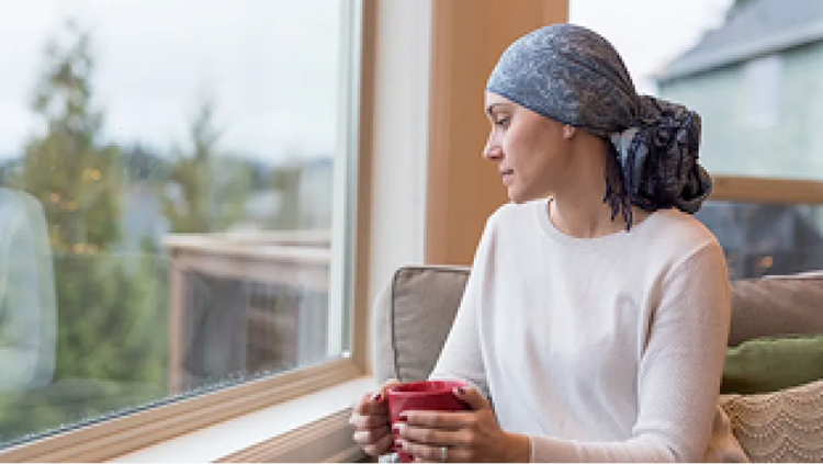 Woman wearing a head covering holding a red mug and looking out a window