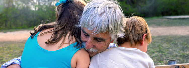 Grandfather hugging two young grandchildren outdoors