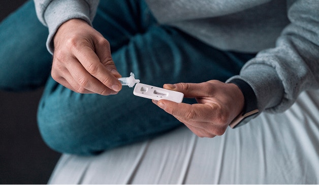 Person adding a sample to a rapid antigen test cassette while seated