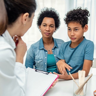 Mother and her preteen son listening to a doctor holding a clipboard during an appointment