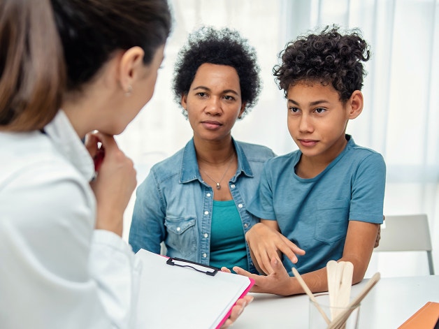 Mother and her preteen son listening to a doctor holding a clipboard during an appointment