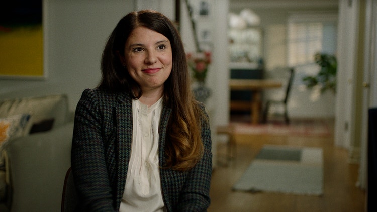 Audrey, actual patient with lung cancer, in a plaid blazer sitting in a living room, smiling