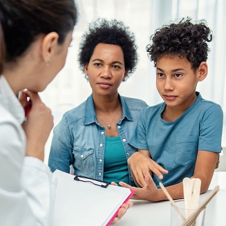 Mother and her preteen son listening to a doctor holding a clipboard during an appointment