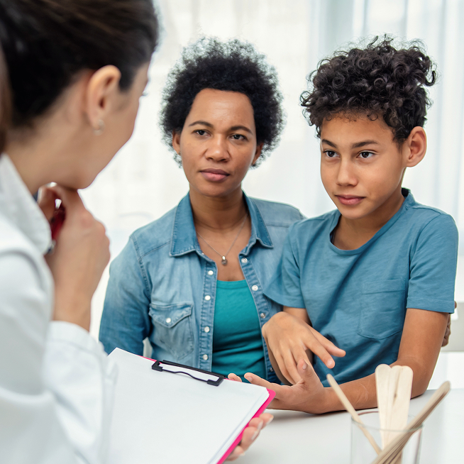 Mother and her preteen son listening to a doctor holding a clipboard during an appointment