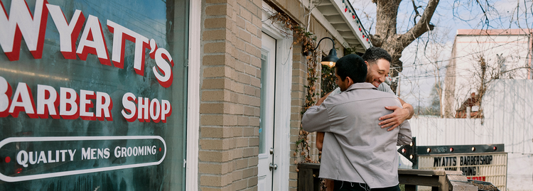 Two men embracing in a friendly hug outside a barber shop