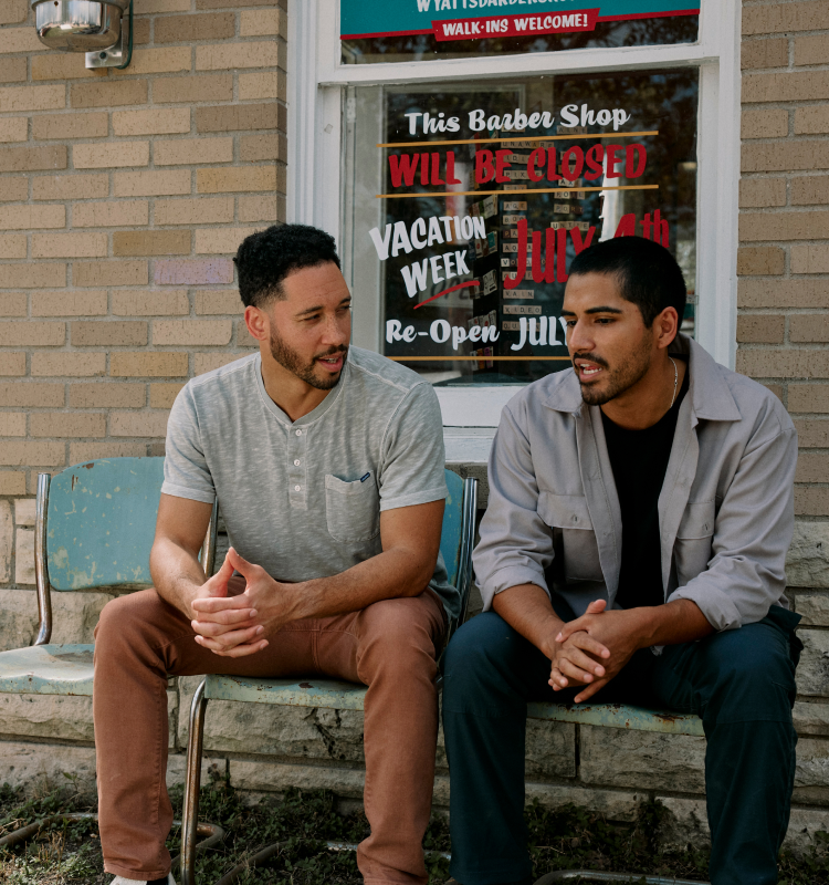 Two men sitting and talking outside a barber shop