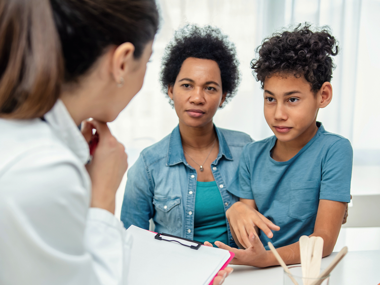 Mother and her preteen son listening to a doctor holding a clipboard during an appointment