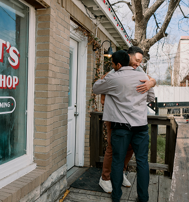Two men embracing in a friendly hug outside a barber shop