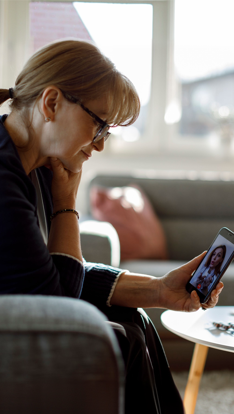 Woman having a video telehealth appointment on her phone with medications and a mug in front of her