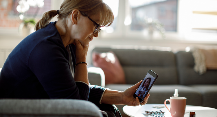 Woman having a video telehealth appointment on her phone with medications and a mug in front of her