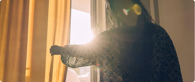 a woman looking out window demonstrating light sensitivity as a migraine trigger