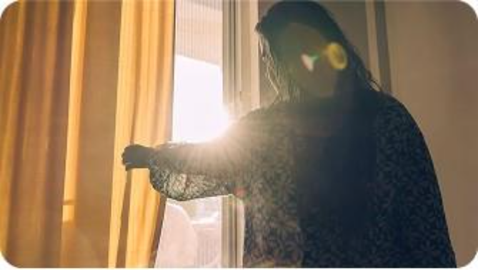 a woman looking out window demonstrating light sensitivity as a migraine trigger