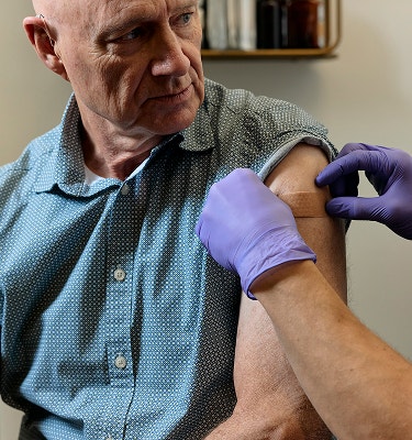 Gloved clinician applying a bandage to an older man's upper arm after a vaccination