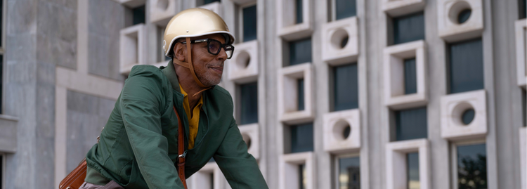 Older man in a gold helmet and green jacket riding a blue bicycle