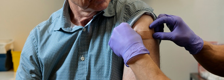 Gloved clinician applying a bandage to an older man's upper arm after a vaccination