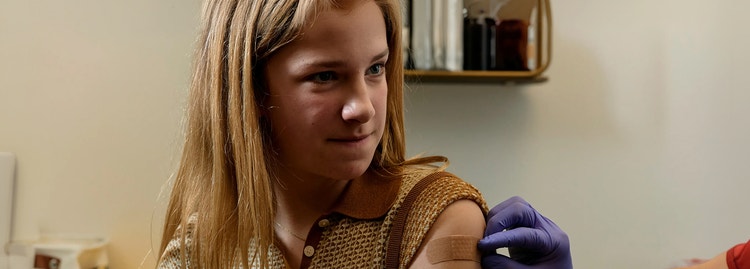 Gloved clinician applying a bandage to a teenager's upper arm after a vaccination