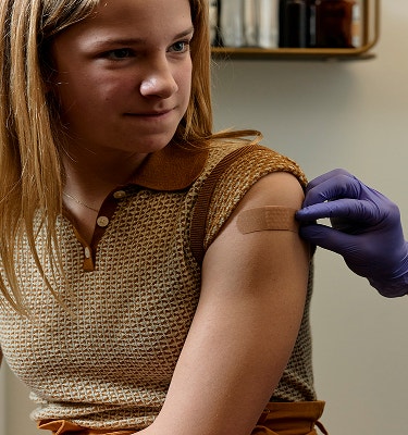Gloved clinician applying a bandage to a teenager's upper arm after a vaccination